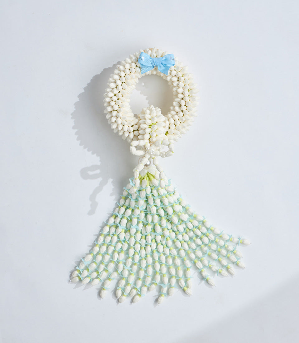 Delicate floral arrangement made of white jasmine flowers arranged in a dress silhouette with blue ribbon bow at the neckline.
