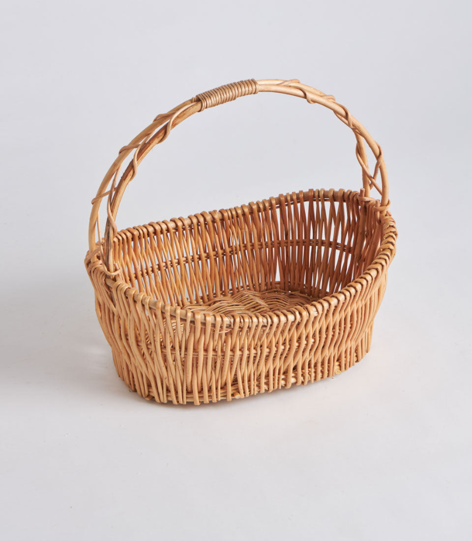 Light brown handwoven oval wicker basket with single arched handle, natural willow material
