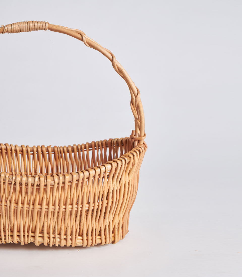 Light brown handwoven wicker basket with arched single handle, natural rattan weave
