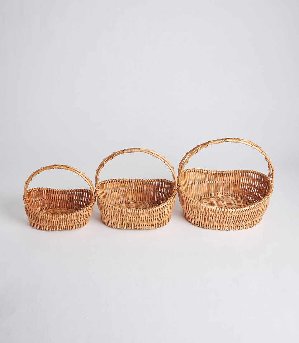 Light brown handwoven oval wicker baskets with arched handles in three sizes