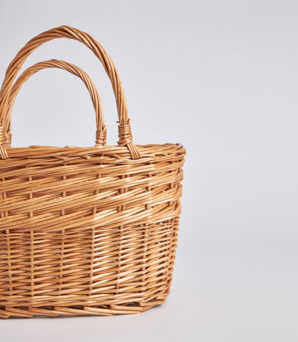 Handwoven natural wicker oval basket with dual arched handles, light brown rattan craft