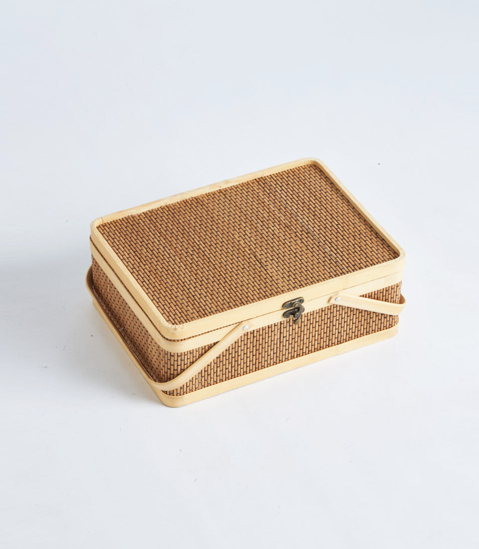 Light brown handwoven rattan gift basket with wood trim, metal clasp, and curved handles