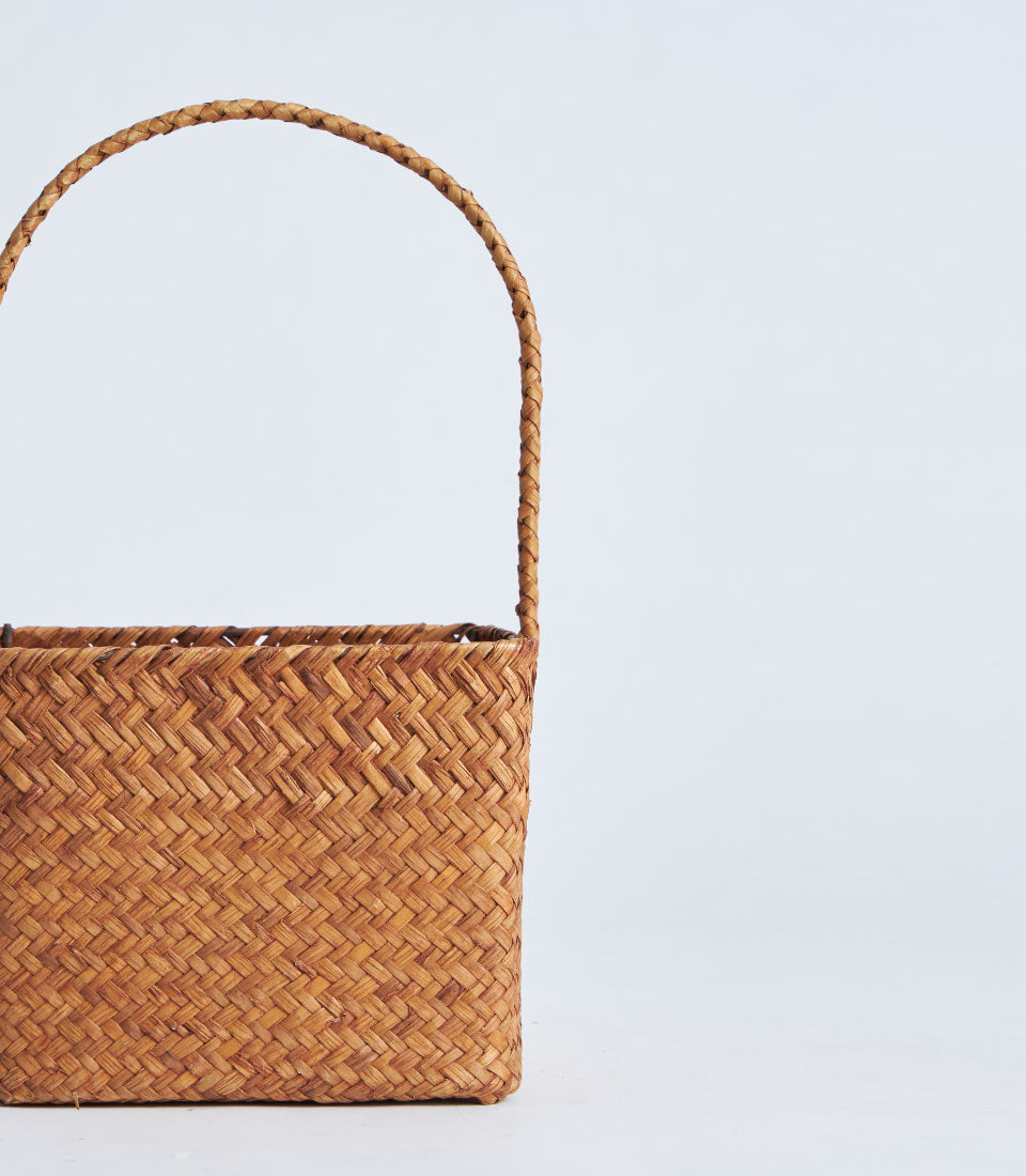Handcrafted natural brown woven rattan basket with braided handle and herringbone pattern