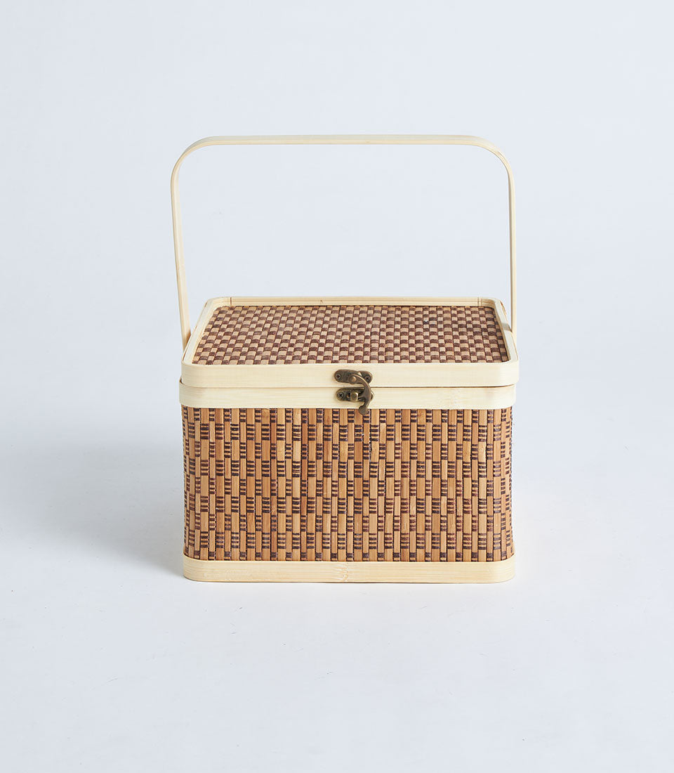 Light brown woven bamboo picnic basket with brass clasp and curved handle, ideal for gourmet gift presentation