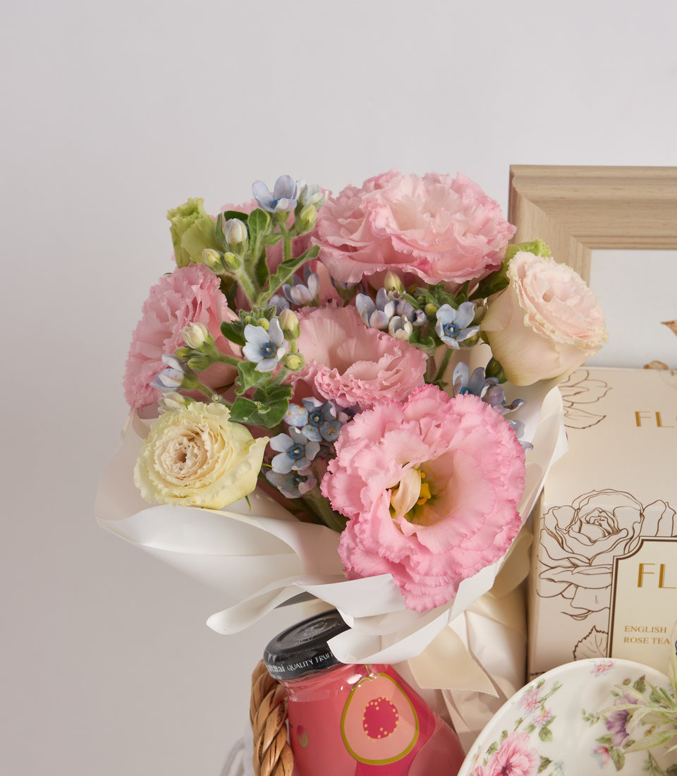 # Alt Text

Pink and cream floral bouquet with carnations and roses, white ribbon, paired with rose tea box and floral teacup on white background.