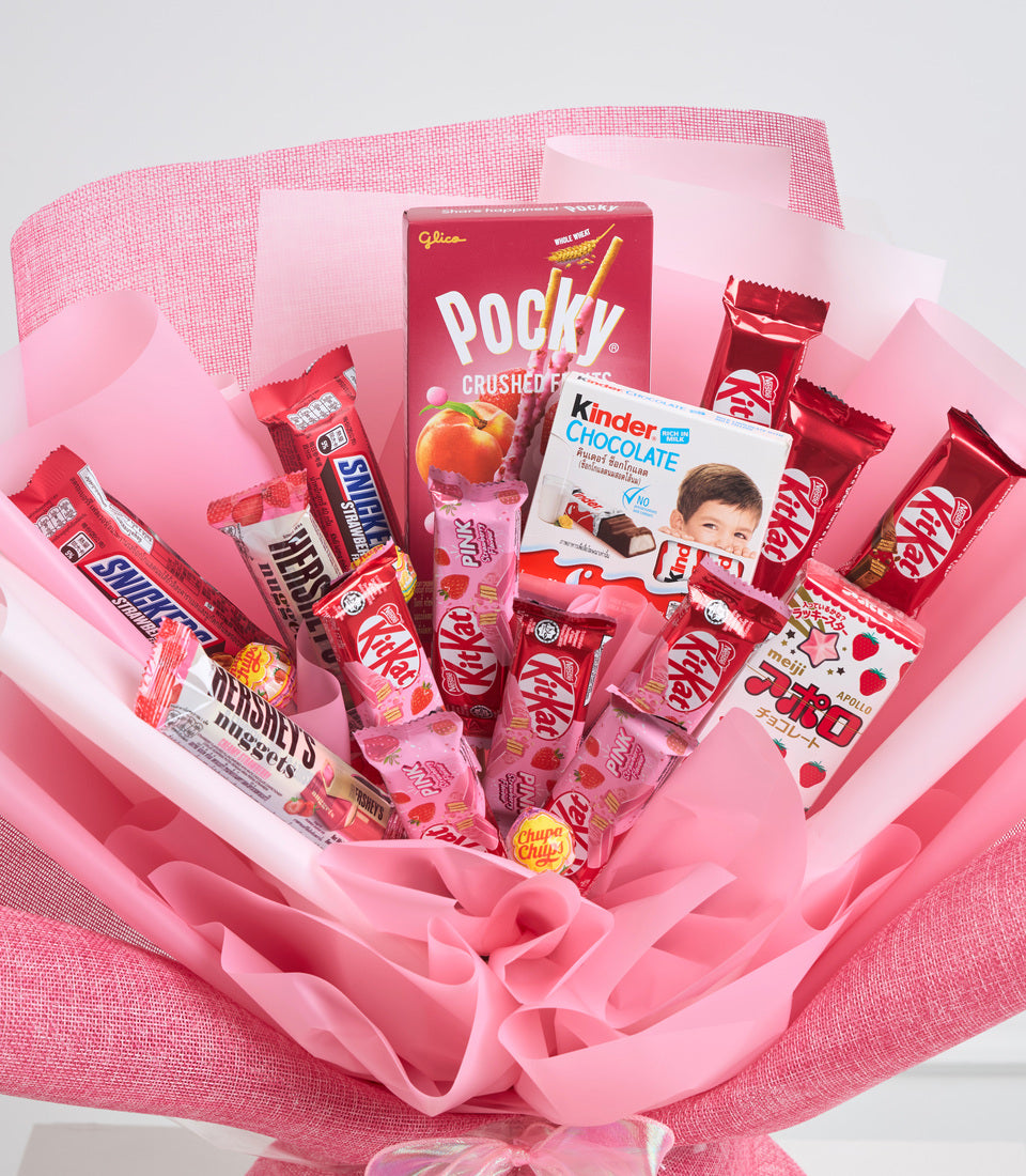 Pink bouquet-style gift arrangement featuring red and pink candy brands including Pocky, Kit Kat, Kinder Chocolate, Skittles, and Smarties, wrapped in pink tissue paper.