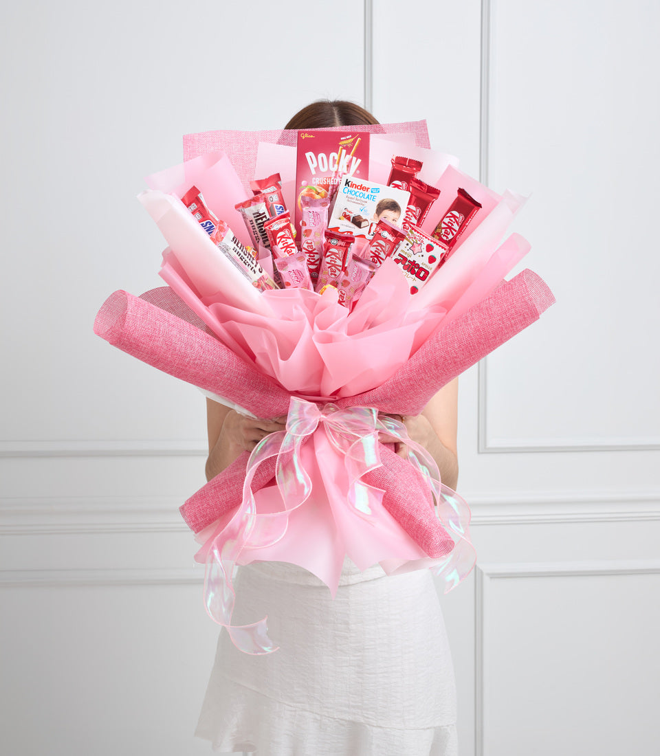 Pink candy bouquet with Pocky, Kinder chocolate, and red snacks arranged in layered pink and white tissue paper wrapping with ribbon bow.