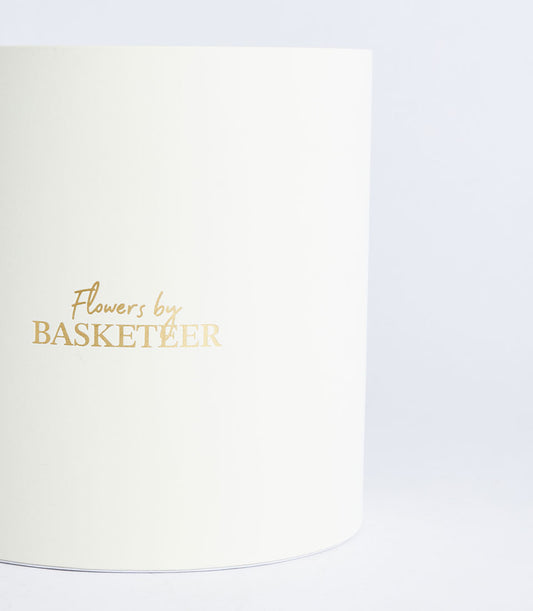 A luxurious ivory round gift box from Basketeer, featuring elegant gold foil "Flowers