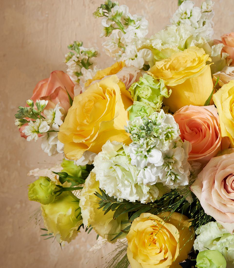 Vibrant yellow and peach rose vase arrangement with white stock and green foliage