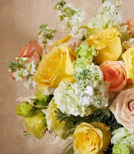 Vibrant yellow and peach rose vase arrangement with white stock and green foliage