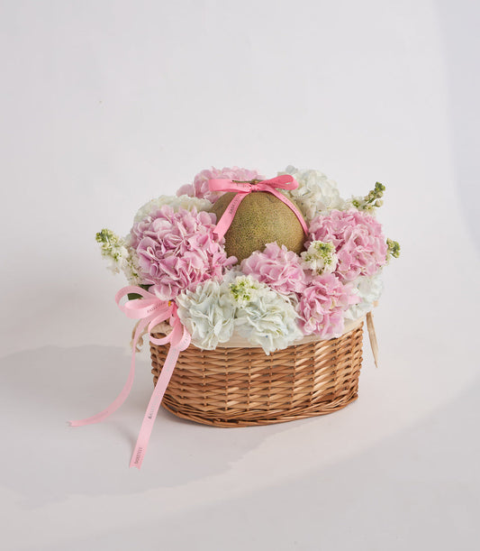 Wicker basket filled with pink and white carnations, baby's breath, and a gold decorative egg with pink ribbon bow.