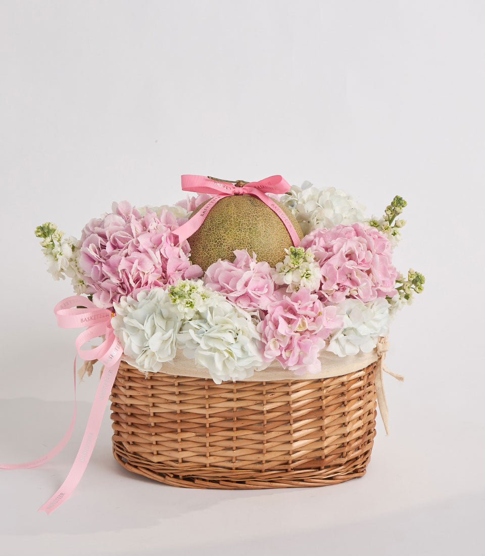Wicker basket filled with pink and white carnations and baby's breath, topped with a gold egg and pink ribbon bow.