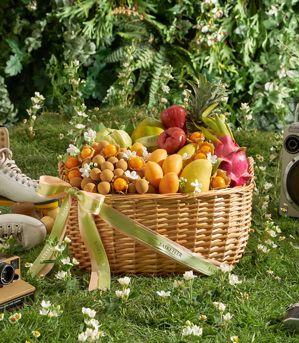 Woven wicker basket overflowing with fresh Thai tropical fruits, mangoes, pineapple, and dragon fruit with green satin