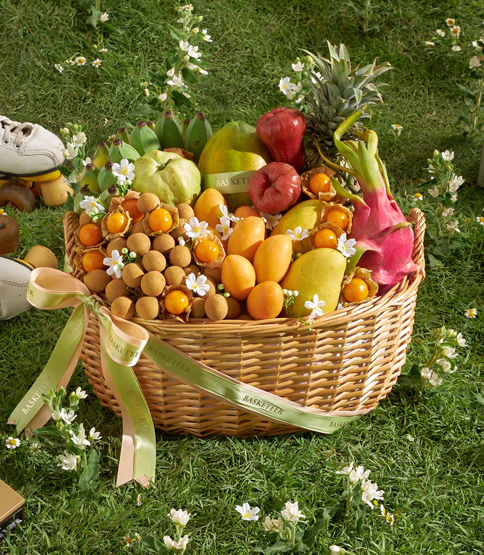 Woven wicker basket overflowing with fresh Thai tropical fruits including mango, papaya, pineapple, dragon fruit, and
