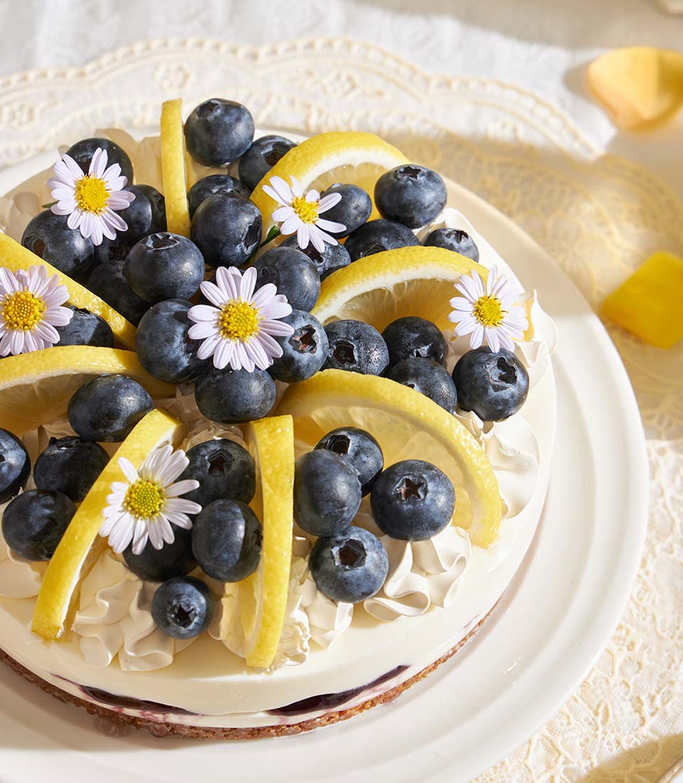 Lemon blueberry Biscoff cheesecake with fresh berries, candied citrus, and edible flowers on white plate
