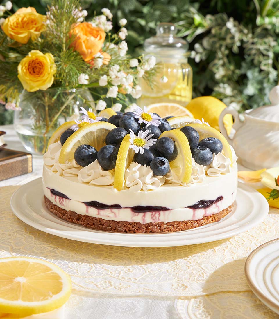 Lemon Blueberry Biscoff Cheesecake with fresh berries, lemon slices, and edible flowers on white plate