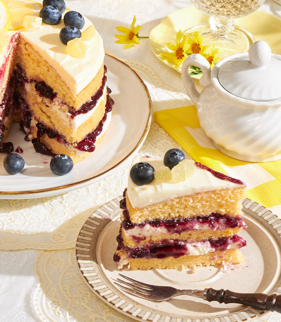 Lemon blueberry layer cake with cream cheese frosting, fresh berries and candied lemon garnish