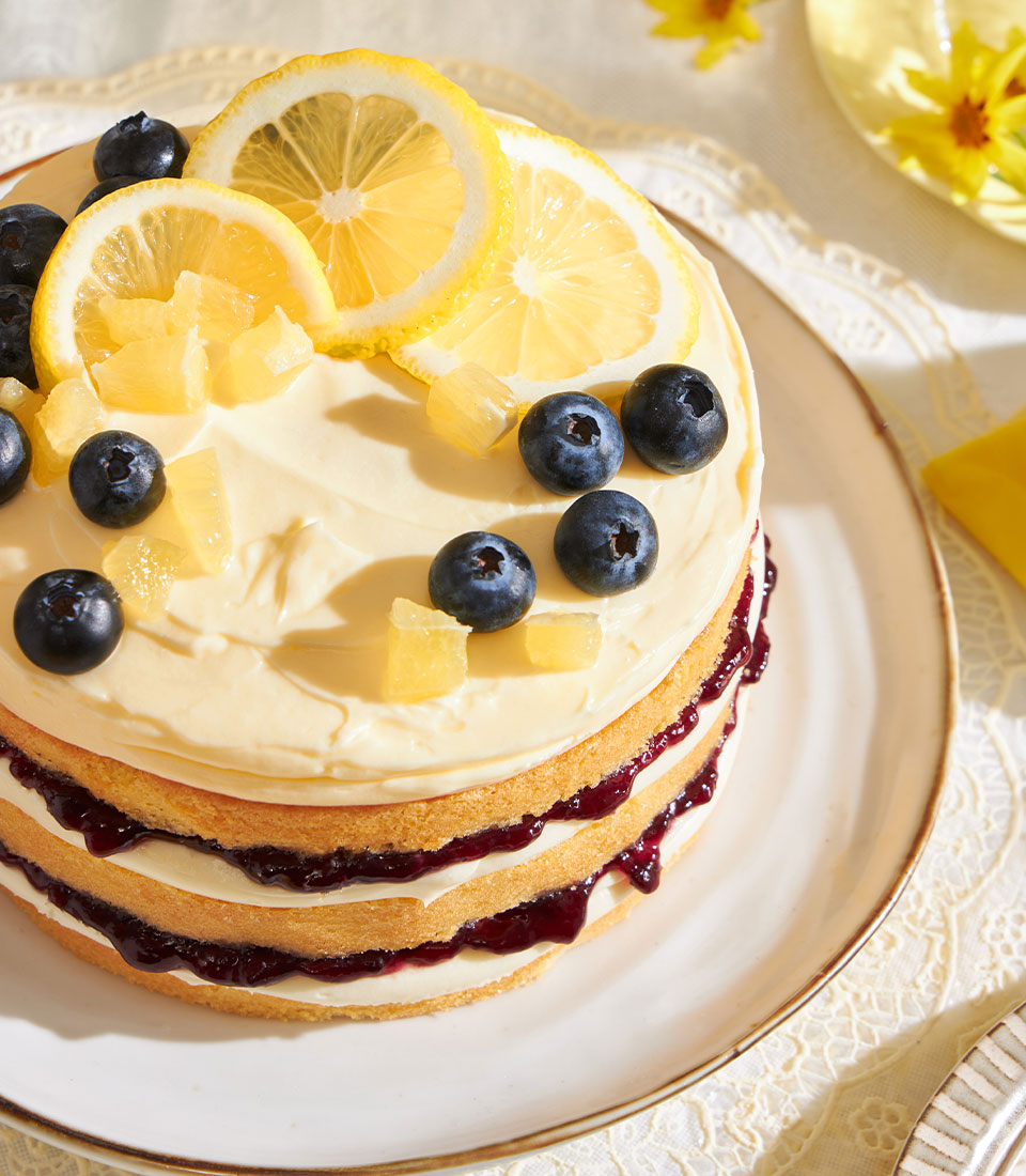 Three-layer lemon blueberry sponge cake with cream cheese frosting, fresh blueberries and candied lemon garnish