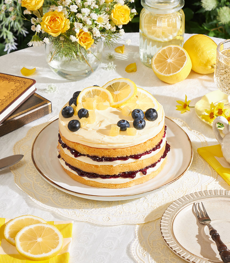 Lemon blueberry layer cake with cream cheese frosting, fresh blueberries and lemon slices on white plate