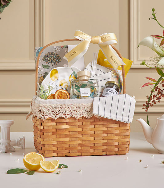 Woven wood gift basket with spa diffuser, honey jar, lemon-motif plate, and wellness essentials with gold ribbon