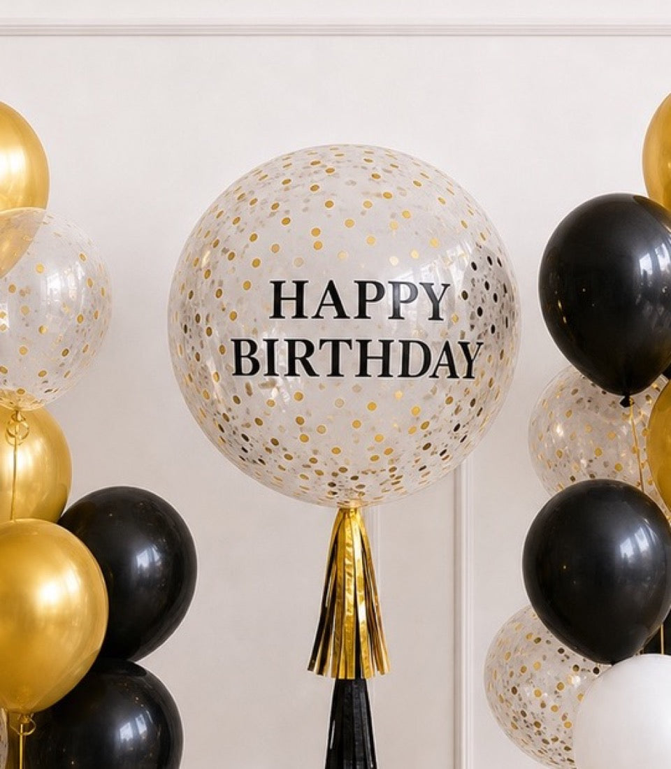 # Alt Text

Large clear balloon with gold confetti and "HAPPY BIRTHDAY" text, surrounded by black and gold metallic balloons with gold tassel.