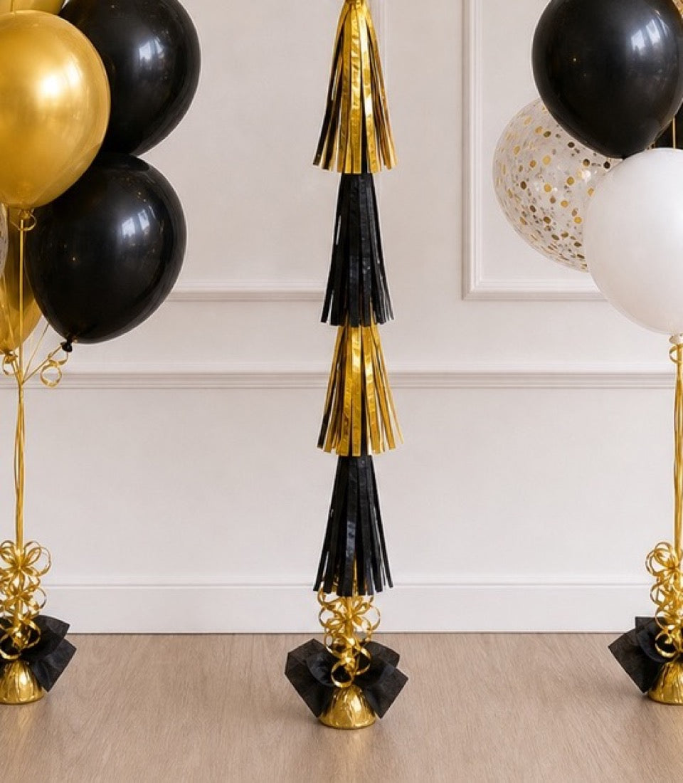 Gold and black balloon tassel garland with black bows on gold bases, elegant party decoration set against white wall.