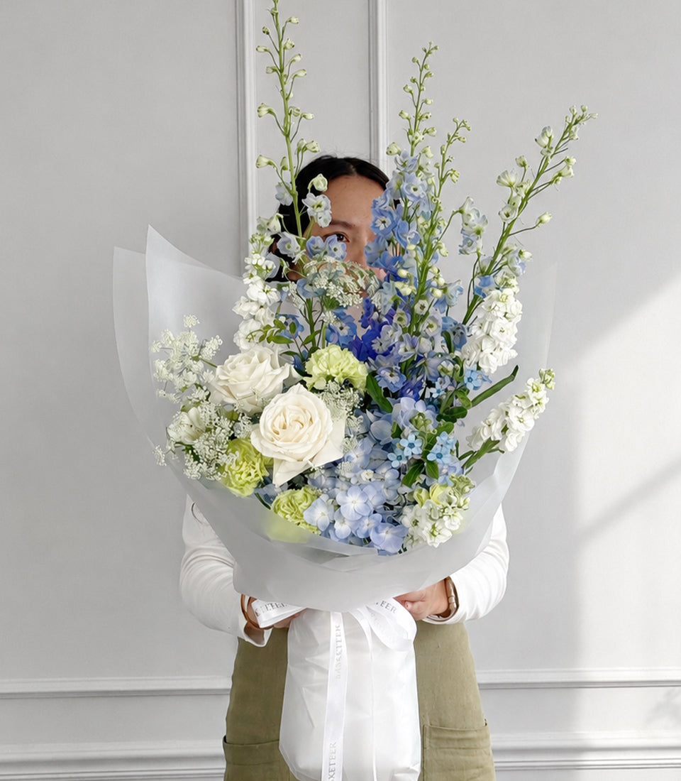 Blue delphiniums, hydrangea and white roses bouquet in white wrapping
