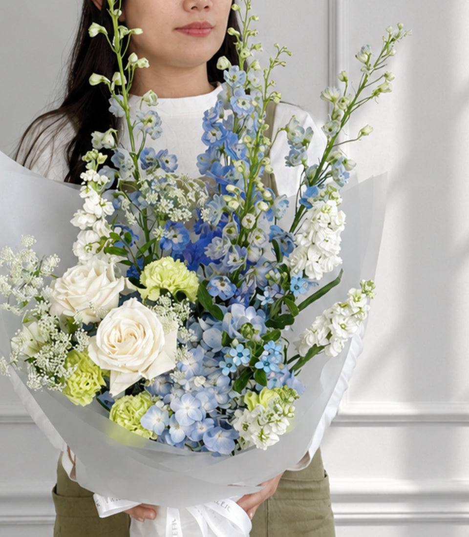 Blue delphiniums, hydrangea and white roses bouquet in white wrapping