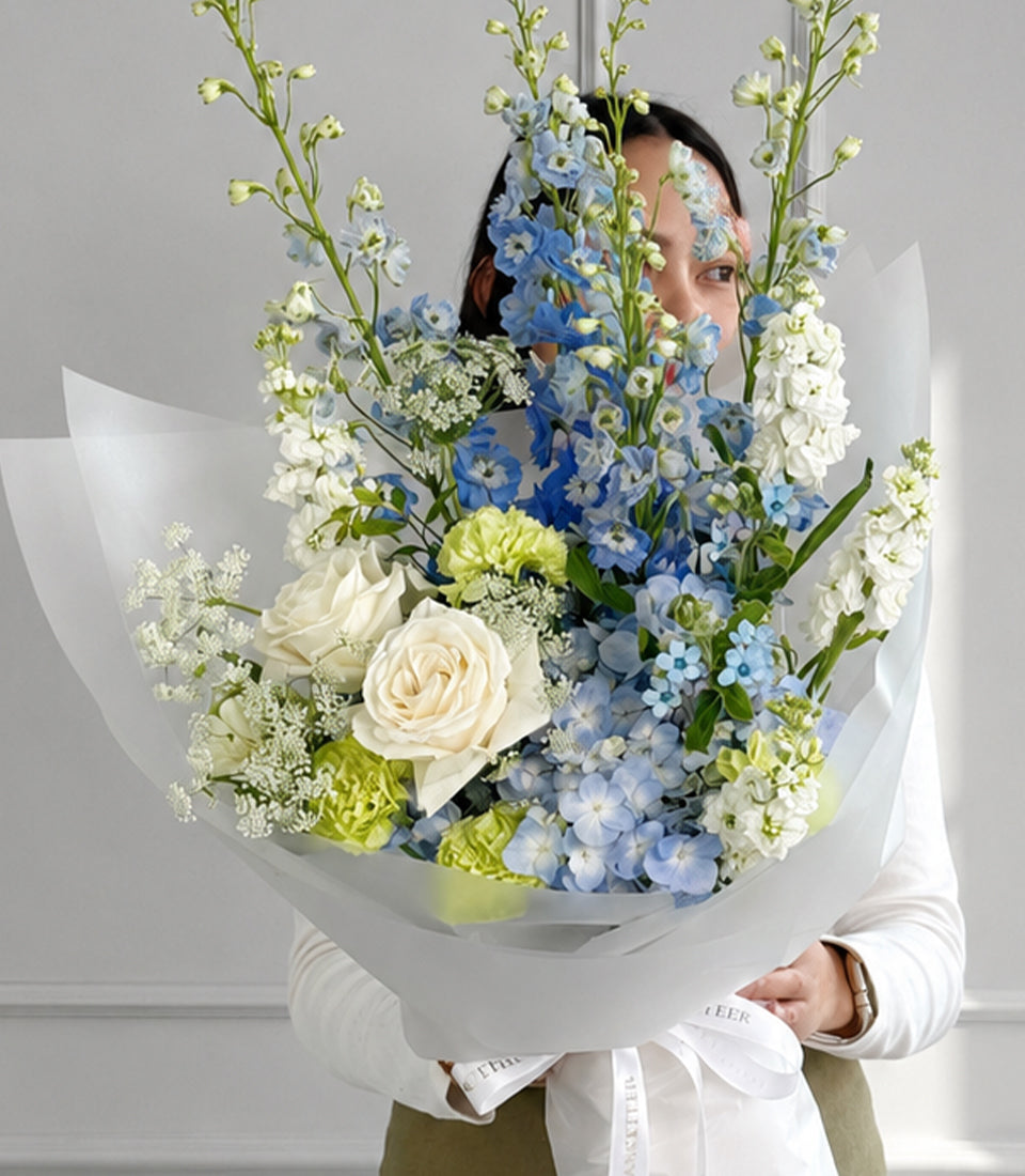 Blue delphiniums, hydrangea and white roses bouquet in white wrapping