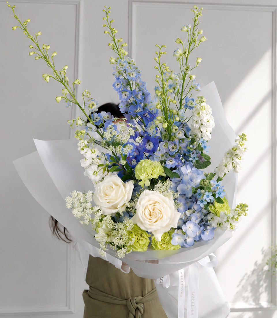 Blue delphiniums, hydrangea and white roses bouquet in white wrapping