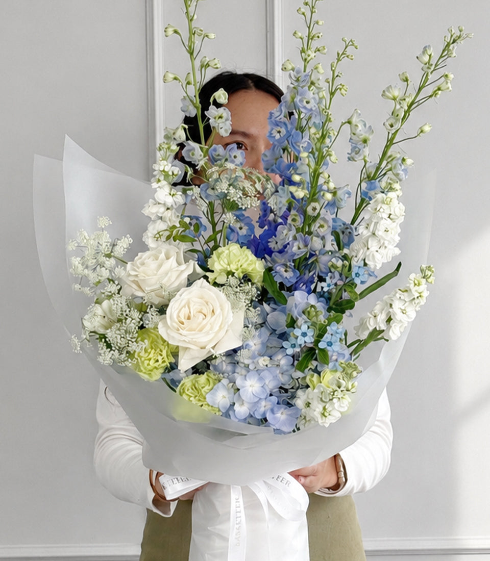 Blue delphiniums, hydrangea and white roses bouquet in white wrapping