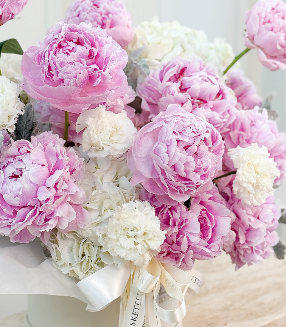 Luxurious bouquet of pink and white peonies with full, ruffled petals, wrapped in white ribbon with Sketerfield branding, displayed in white vase.