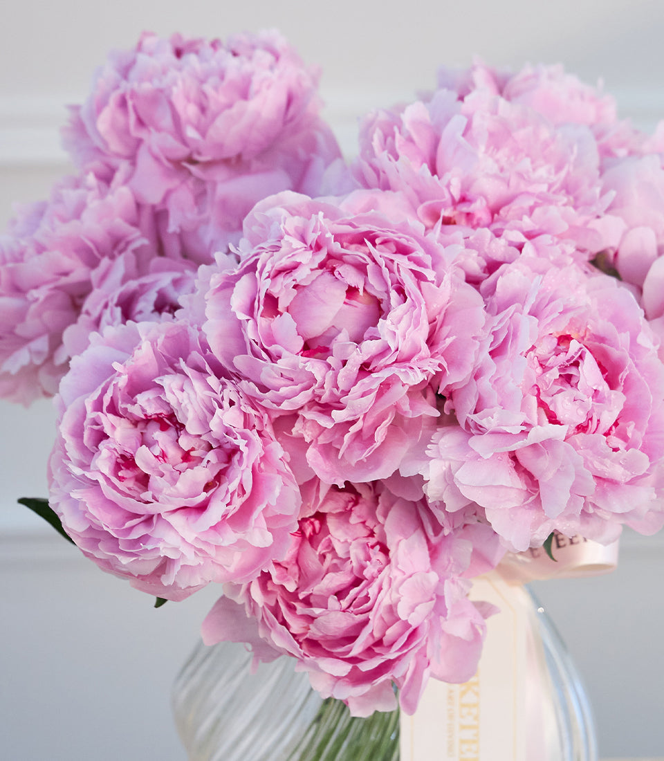 Elegant arrangement of lush pink peonies in a textured glass vase, adorned