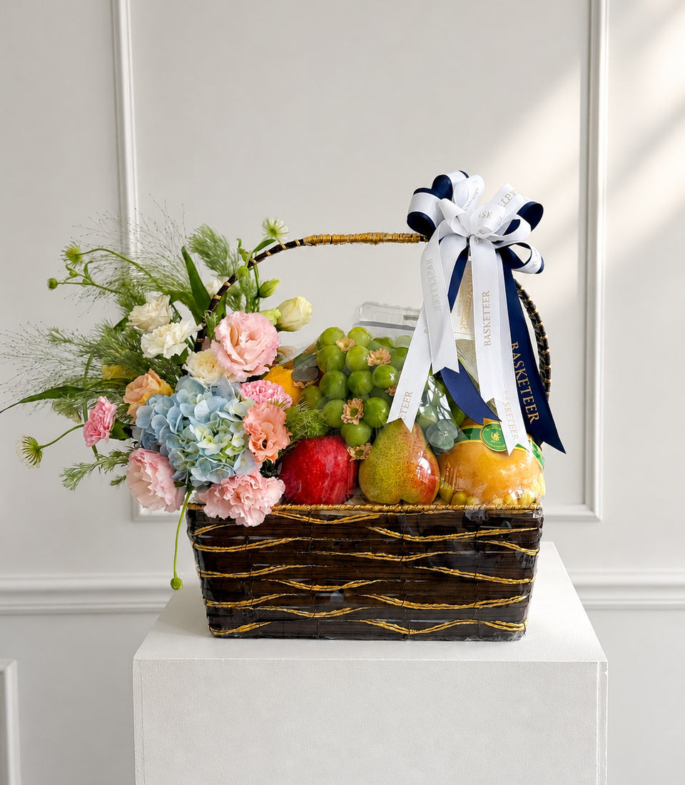 # Alt Text

Luxury gift basket with black woven base, gold accents, fresh flowers in pink and blue tones, assorted fresh fruits, and navy/white ribbon bow.