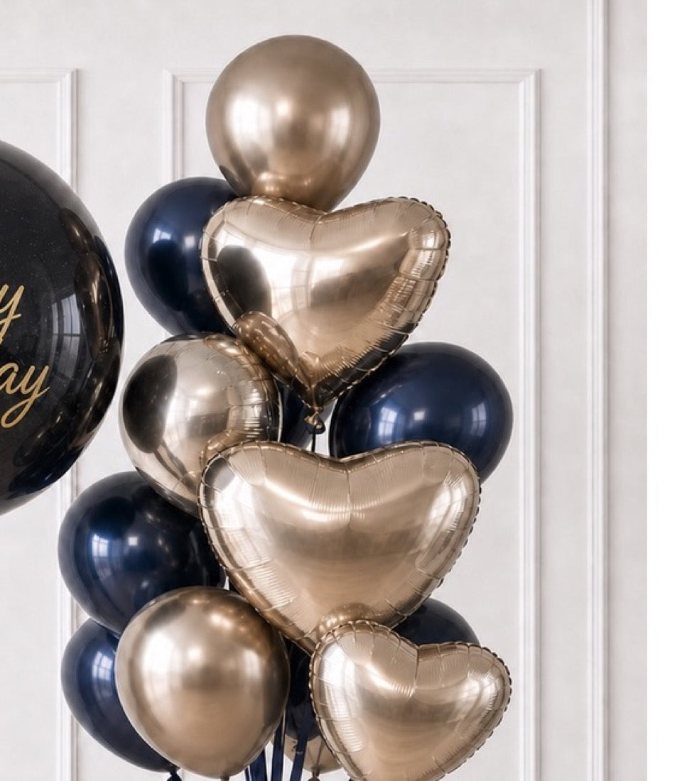 Elegant balloon bouquet with champagne heart-shaped foil balloons, navy blue and champagne spheres, arranged vertically against white paneled wall.