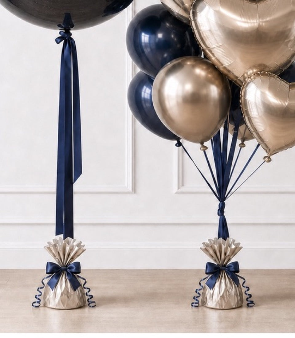 Navy and champagne balloon bouquet with metallic spheres, foil balloons, navy ribbons, and pleated base weights with bows.