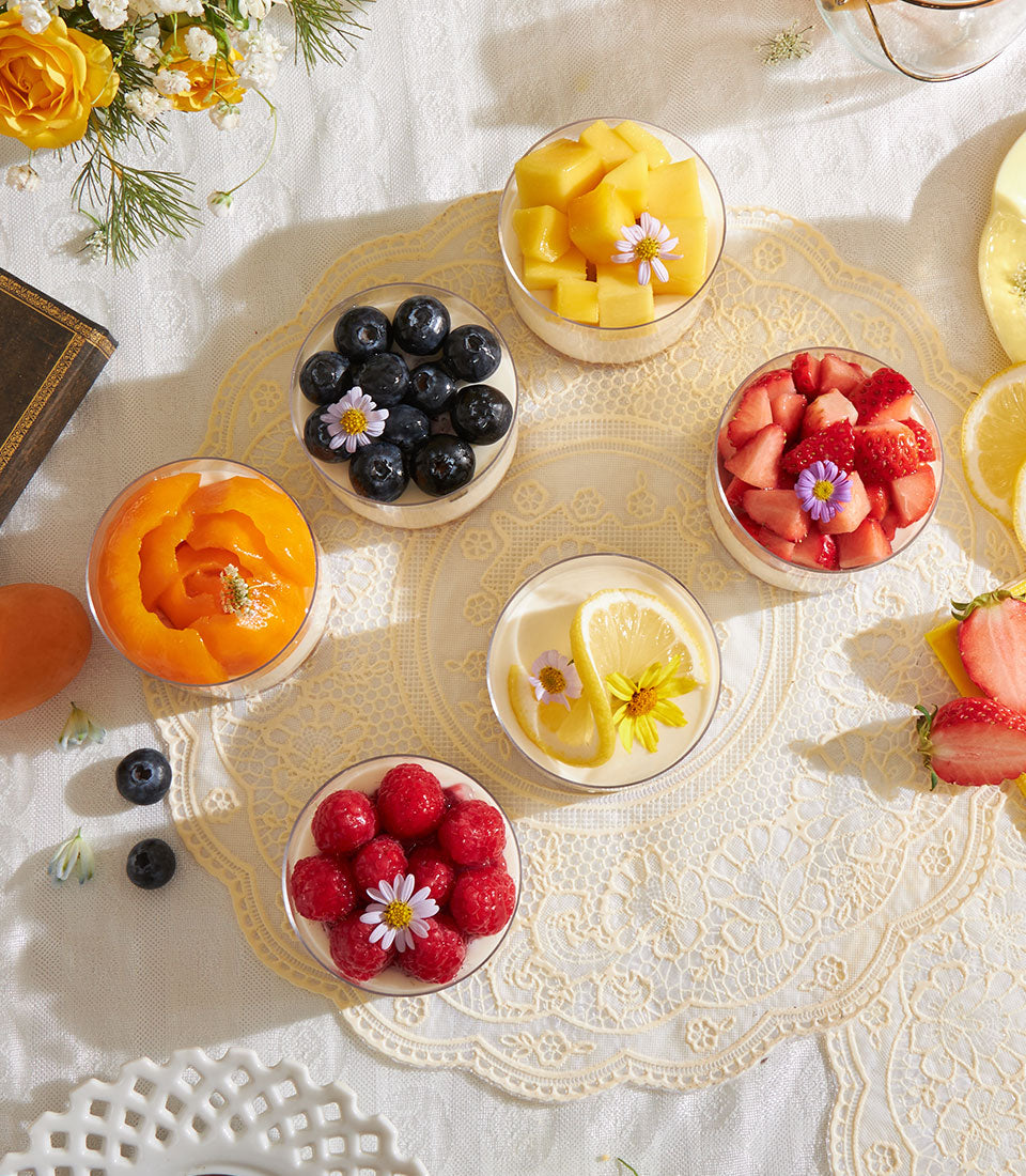 Mini cheesecake cups with Biscoff base and assorted fresh fruit toppings, arranged on lace doily