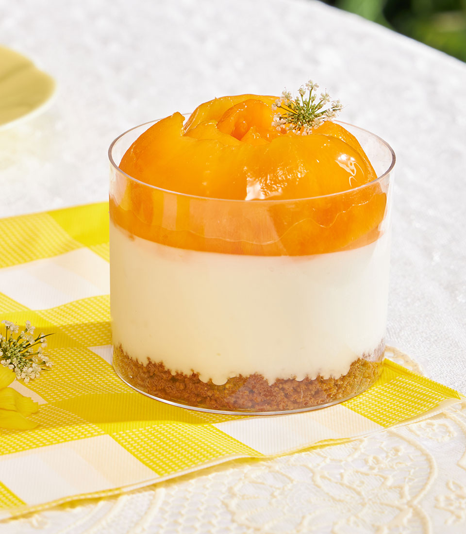 Mini cheesecake cup with Biscoff base, creamy filling, and fresh peach topping in clear glass