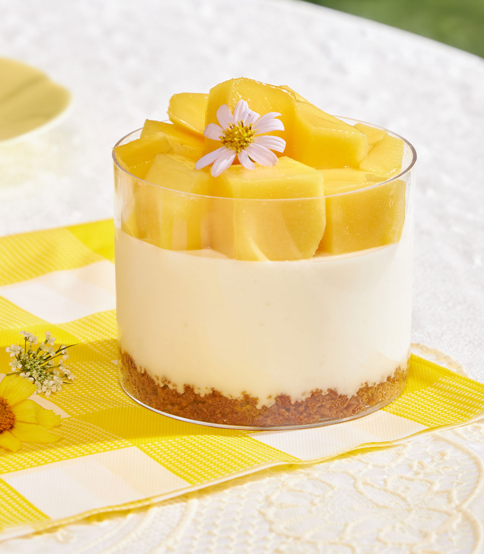 Mini cheesecake cup with Biscoff base, mango topping, and edible flower garnish in glass