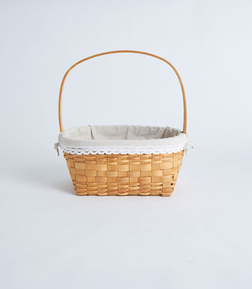 Light brown handwoven rectangular wicker basket with wooden handle and beige polka-dot fabric liner