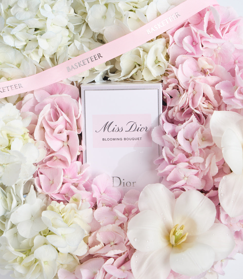 Miss Dior Blooming Bouquet perfume box surrounded by pink and white peonies and hydrangeas with pink Basketeer ribbon.