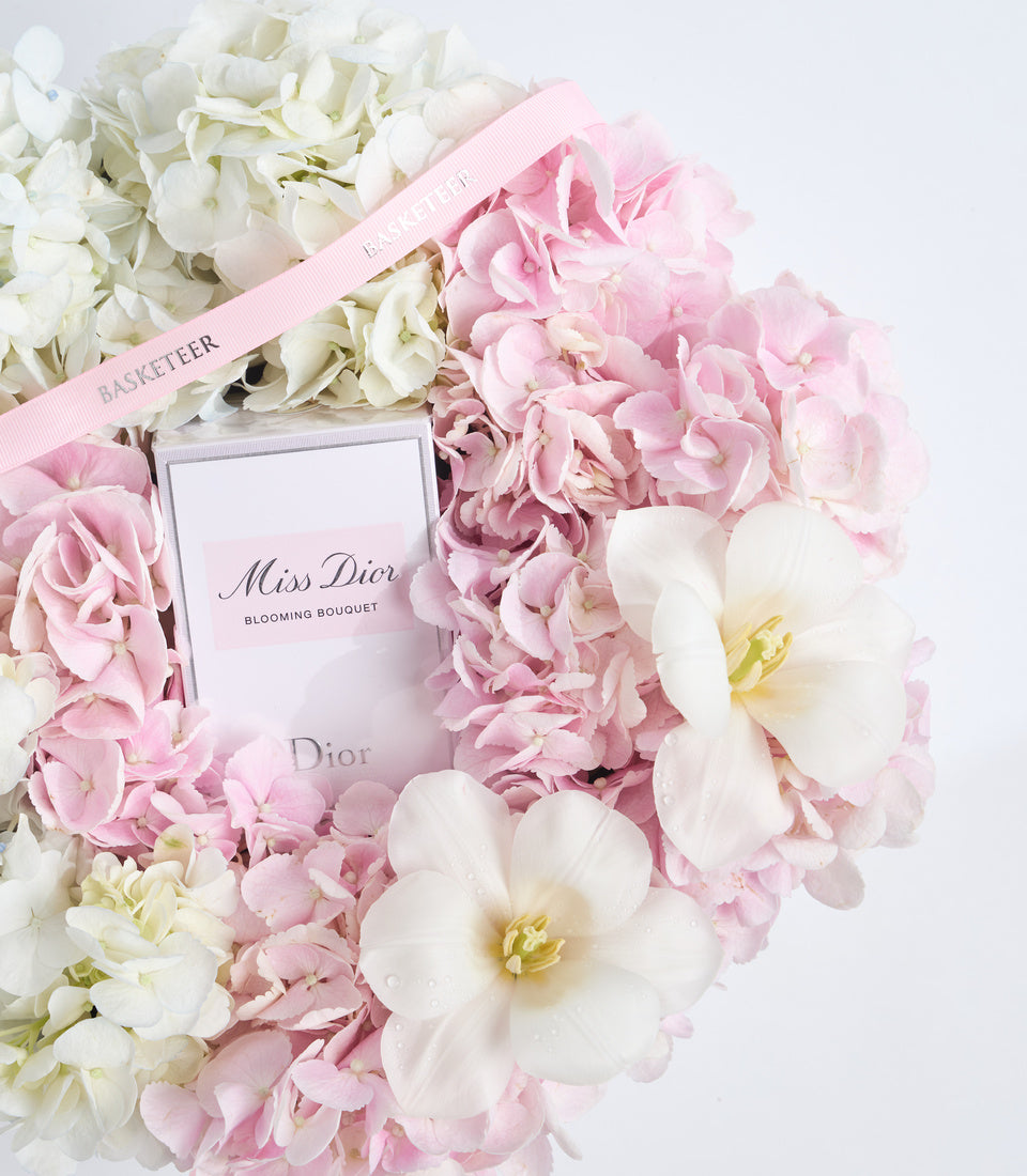 Miss Dior Blooming Bouquet perfume surrounded by pink and white flowers with a pink ribbon on white background.