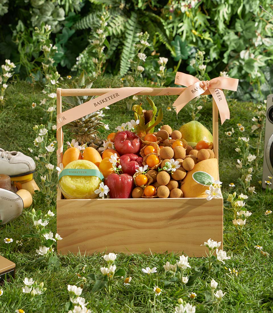Wooden crate tropical fruit gift basket with apples, oranges, pineapple, mangoes, and longan, tied with pink ribbon
