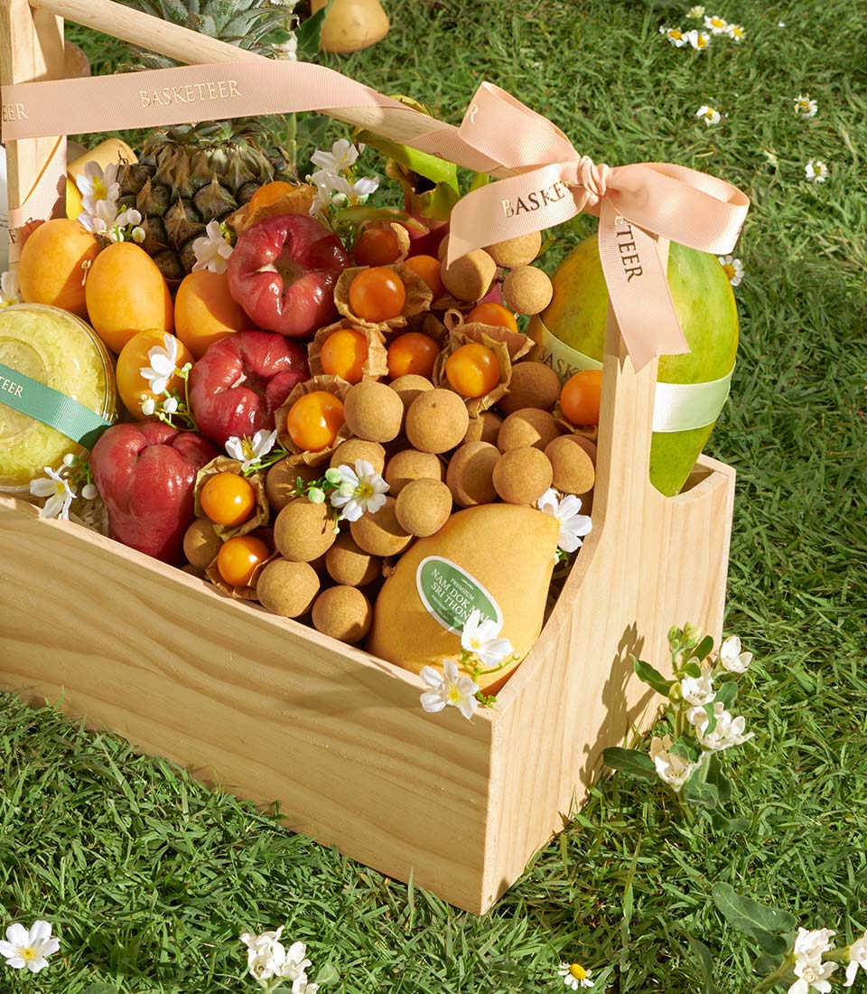 Premium Thai tropical fruit basket with mango, longan, and rose apples in wooden crate with pink ribbon