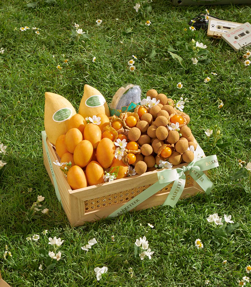 Wooden gift basket with Nam Dok Mai mangoes, longan, golberries, and chocolate-covered treats on green grass