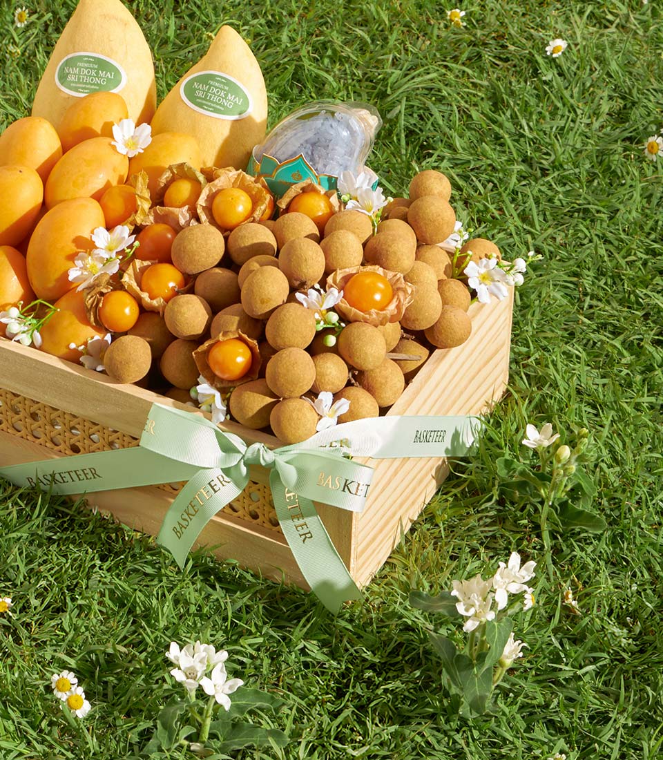 Wooden gift basket with Nam Dok Mai mangoes, longan, and physalis fruits on green grass