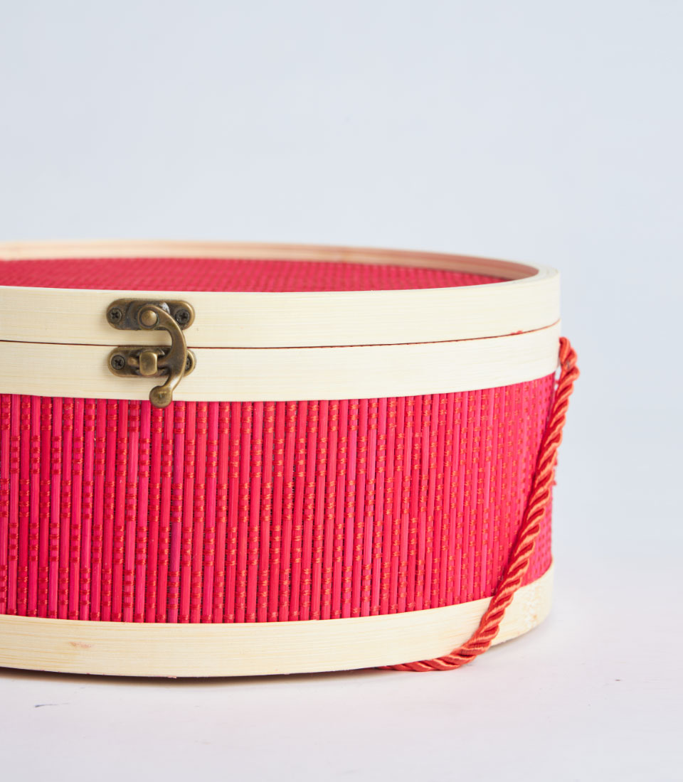 Vibrant fuchsia woven gift basket with wood trim, brass clasp, and twisted red-gold handle