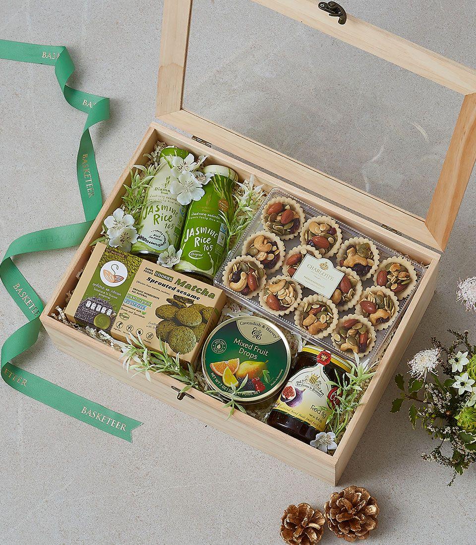 Wooden gift box with gourmet treats, matcha cookies, fig spread, rice, and nut tarts on white shredded paper