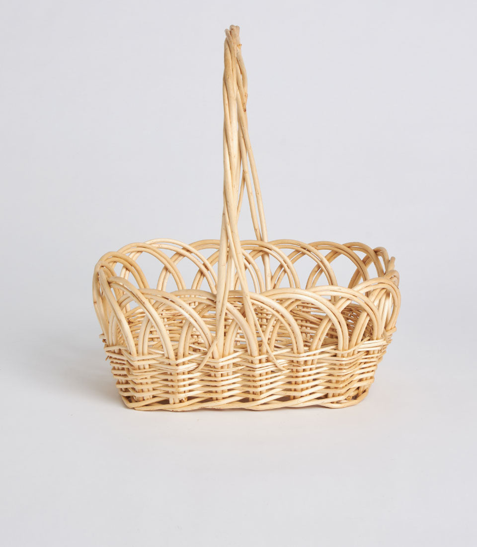 Light beige handwoven oval wicker basket with tall arched handle, artisan gift hamper base
