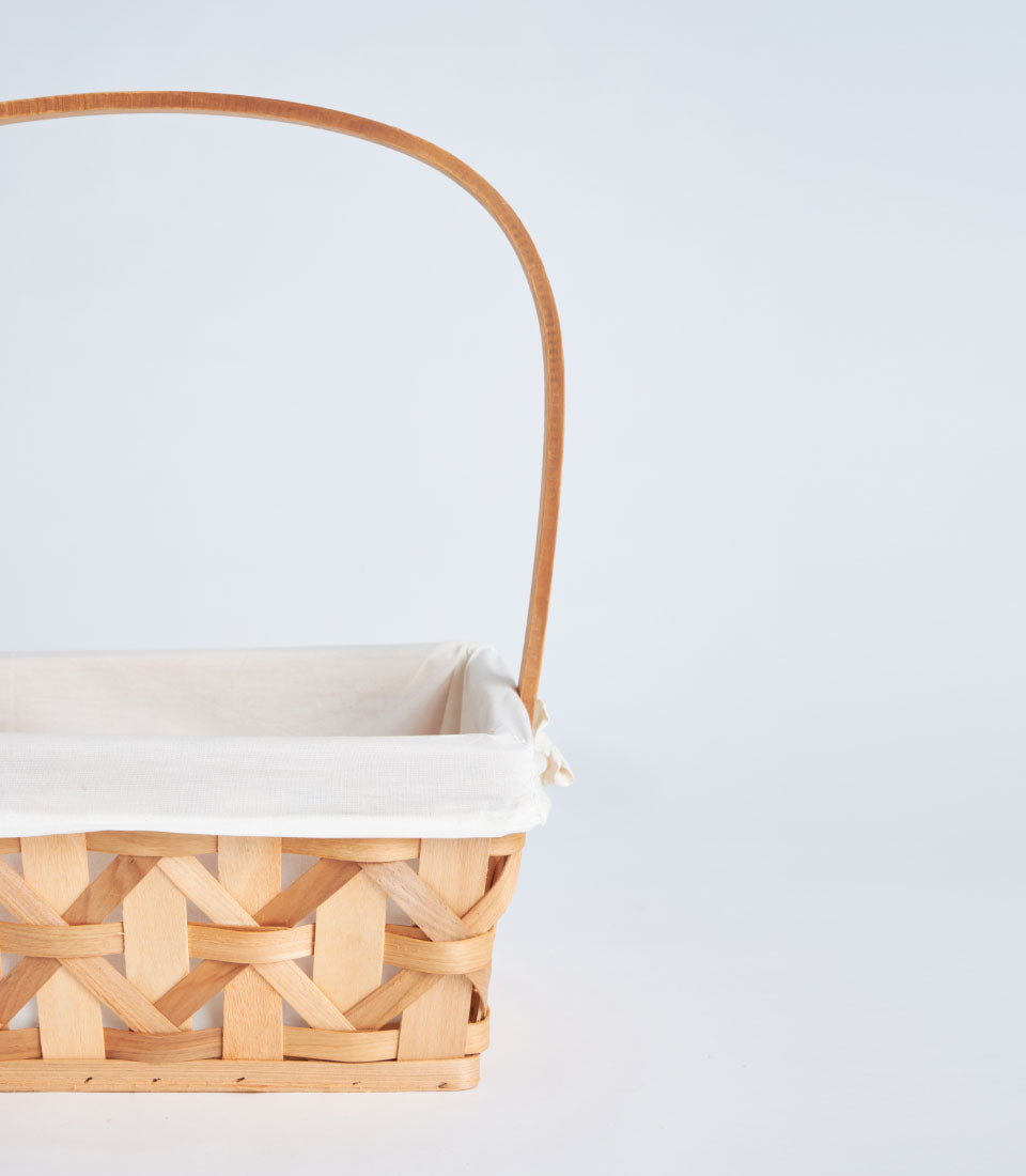Natural woven wicker basket with arched handle and cream fabric lining for luxury gift hampers